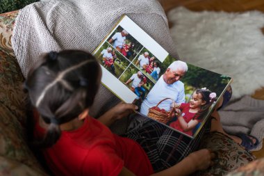 Elinde fotoğrafları olan küçük beyaz bir kız elinde bir fotobook tutuyor..