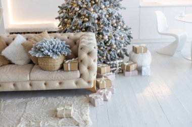 Yeni yıl ağacının süslendiği klasik bir beyaz noel iç mimarisi. Gri sandalye ve hediyeler ağacın altında.