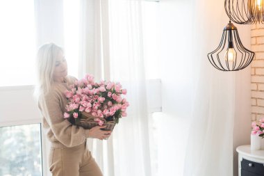 Genç ve zarif bir kadın elinde bahar çiçekleriyle çiçek sepeti tutuyor..