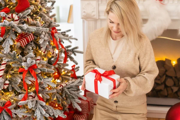 Curious happy romantic woman standing against Christmas tree background. Cheerful lady surprised of the present after the opening in the gift box. Marry Christmas and Happy Holidays