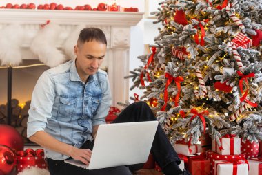 Serbest çalışan genç bir adam internet üzerinden ev ofisteki kediyle bilgisayardan video görüşmesi yapıyor. Noel havası, yılbaşı süsü, Noel tatili. Tecrit