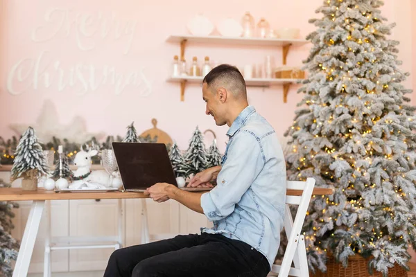 自宅のオフィスで猫とノートパソコンのコンピュータ上でビデオ通話を持つ若い男のフリーランスの作業距離をオンラインで クリスマス気分 新年の装飾 クリスマス休暇 ロックダウン隔離 — ストック写真
