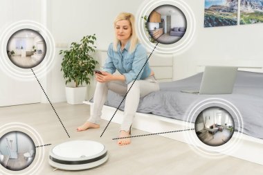 Akıllı telefonlarda akıllı ev uygulaması kullanan mutlu genç bir kadın ve modern oturma odasının arka planındaki robot süpürge zemini.