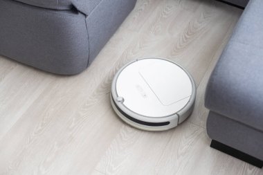 Robot elektrikli süpürge plastik zeminde sürücüler ve dökülen karabuğdayı temizler. Akıllı Ev. Ev asistanı kavramı.