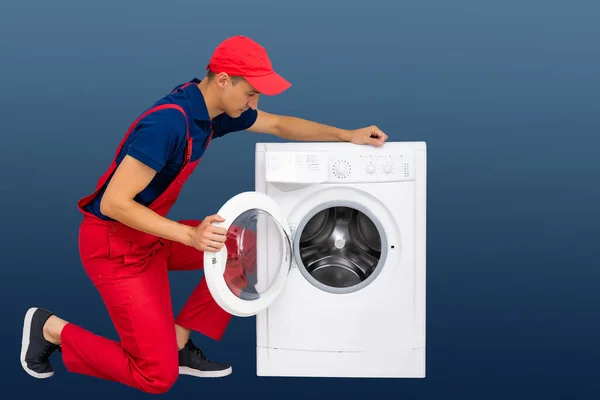 Tamirci Mavi Arka Planda Bir Çamaşır Makinesini Tamir Ediyor — Stok fotoğraf