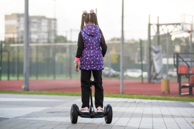 Dışarıda elektrikli scooter 'ın üzerinde duran mutlu küçük kız..