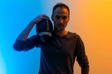 Handsome young man with rugby ball on color background