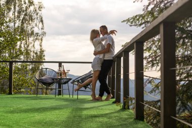 Balkondaki çift, dağların arka planına karşı. Hayat terası oldukça mutlu bir yaz evi.