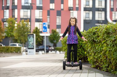 Elektrikli scooter kullanan küçük bir kız. Kişisel çevre taşımacılığı, jiroskoplu scooter, akıllı denge çarkı. Popüler elektrik taşımacılığı.
