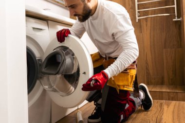 Usta bozuk çamaşır makinesini tamir ediyor..