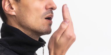 Bad breath. The concept of halitosis. A young man checks his breath with his hand.