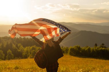 Genç, mutlu, uzun saçlı Amerikalı kadın rüzgârda sallanıyor. Amerikan bayrağı üzerinde. Açık havada dinleniyor, sıcak yaz gününün tadını çıkarıyor..