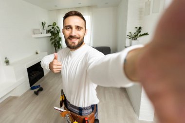 Yakışıklı, neşeli tamircinin portresi. Akıllı telefondan selfie çekiyor. Gömlek ve tulum giyiyor..