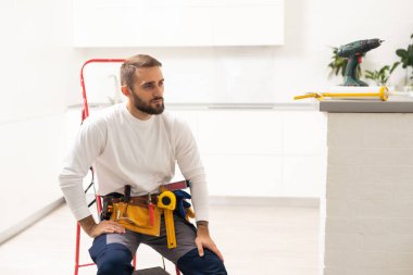Ev tamiri. Metal merdivenli profesyonel erkek tamircinin portresi. İş yerinde gülümseyen adam, tamiratı bitirdiği odanın ortasında duruyor.