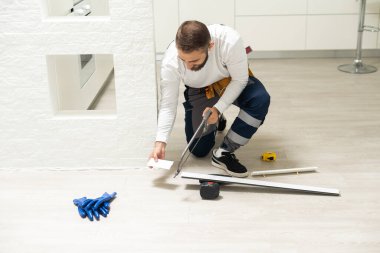 A man installs a floor skirting board. Fixing the plastic skirting board with screws to the wall. Home renovation