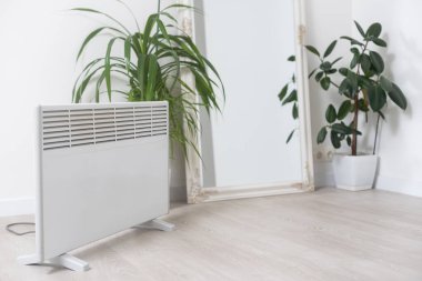 Gri arka planda bitki ve elektrik ısıtma bataryası, ev bitkileri konsepti için kuru havaya zarar verme, ısıtma mevsimi.
