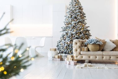 Yeni yıl ağacının süslendiği klasik bir beyaz noel iç mimarisi. Gri sandalye ve hediyeler ağacın altında.