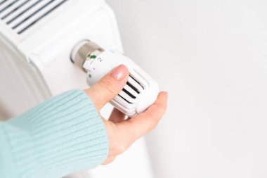 Bir kadın eli beyaz bir ısıtıcıya tutunuyor. Isıtma kavramı.