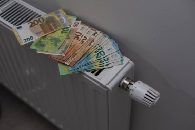 Expensive heating costs. Paying bills. Euro money paper banknotes falling into heating radiator battery at home