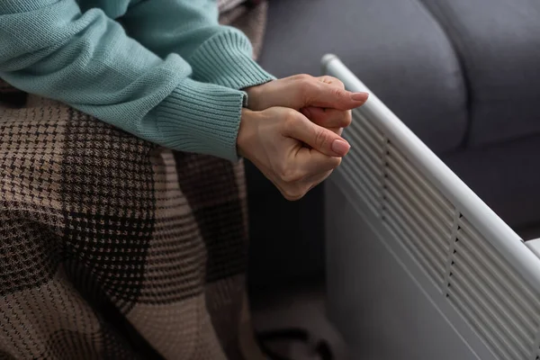 Woman warming hands near electric heater at home, closeup.