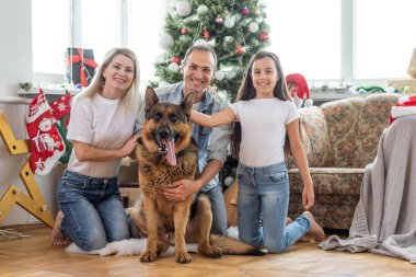 Heyecanlı kız ve ailesi Noel ağacının yanında oturmuş gülümsüyor. Noel zamanı aile.