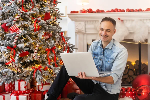 ノートパソコンを使ったハンサムな男ビデオチャット電話で話してオンラインで買い物 背景にクリスマスライト — ストック写真
