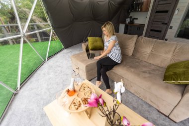 Kafkasyalı genç bir kadın, kubbe kamp otelinde dizüstü bilgisayarını kullanıyor ve izliyor. Turizm, tatil ve hafta sonu