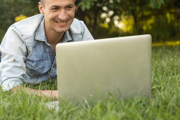 在花园里工作的带着笔记本电脑的自由职业者坐在户外草坪上的椅子上 年轻的博主男性在公园的电脑上工作 为社交媒体制作视频 工作地点 远程工作 — 图库照片