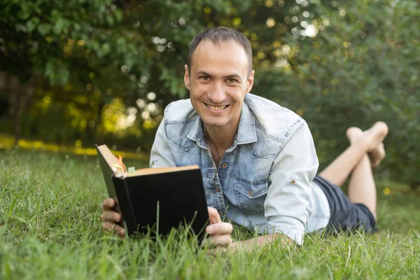 Genç adam çimenlerde uzanıyor, rahatlıyor ve kitap okuyor..