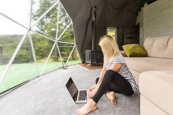 stock image Happy young woman chatting online by using laptop in dome camping. Glamping vacation concept.