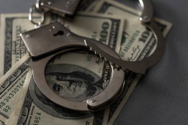 Kelepçeler beyaz arka planda izole edilmiş 100 dolarlık banknotların üzerinde..