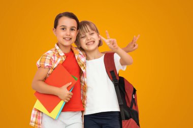 İki küçük kız öğrencinin fotoğrafı. Kız kardeş sınıf arkadaşlarının elinde izole edilmiş turuncu arkaplan kitapları var..