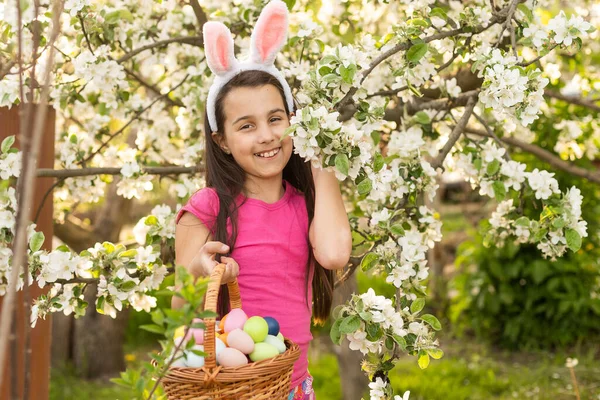 かわいい子女の子のイースターの日にバニーの耳を着てします 女の子は家の近くの芝生の上のイースターの卵狩り 塗装卵のバスケットを持って女の子 — ストック写真