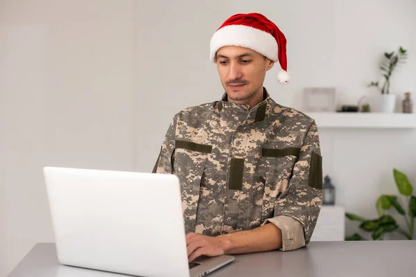 ノートパソコンを持ったサンタの帽子の軍人 — ストック写真