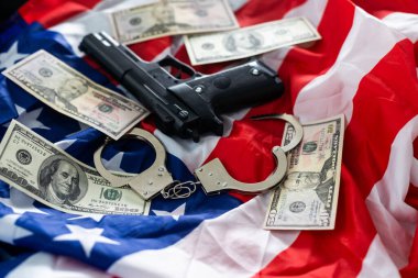 Gun, holster, handcuffs and cash in front of the American flag.