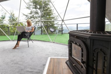 Orta yaşlı bir kadın tatillerde Glamping 'lerin evinde dizüstü bilgisayar kullanıyor. Tatil çadırı. Rahat, kamp, hygge, yaşam tarzı konsepti.