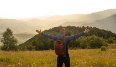 Genç adam dağın tepesindeki manzaranın tadını çıkarıyor. Karpat Dağları, Ukrayna.