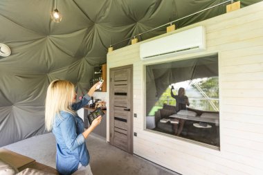 Young woman using smartphone home application on tablet computer when setting temperature in her apartment.
