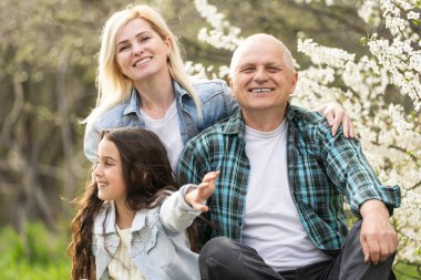 Aile parkta piknik yapıyor, bahçesinde çiçek açan ağaçlar, bahar.