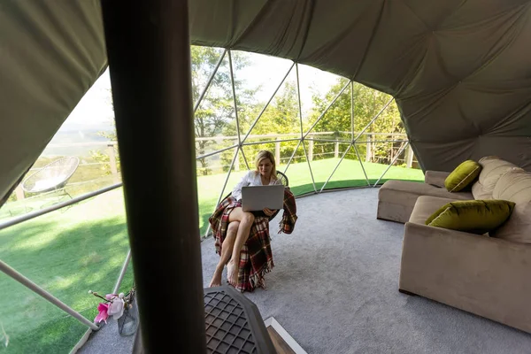 在笔记本电脑地理穹顶帐篷上工作的妇女 蓝色背景 度假生活方式的概念 户外小木屋 风景秀丽 — 图库照片