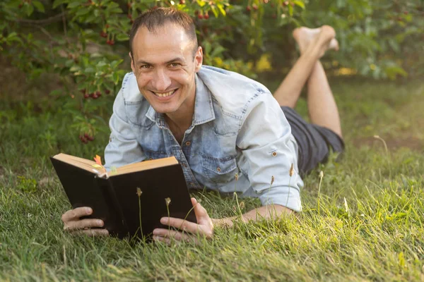 stock image Man reading a book on the grass.