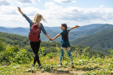 Mother and child with a backpack enjoying in the mountains.The concept of family travel, adventure, and tourism. Lifestyle and hiking autumn vacations outdoor. Back view