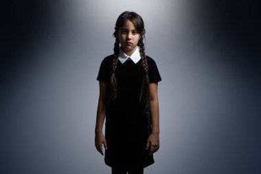 Cadılar Bayramı 'nda Çarşamba Addams kostümlü küçük bir kızın portresi. Ciddi ifade ve karanlık arkaplan ile karanlık atmosfer