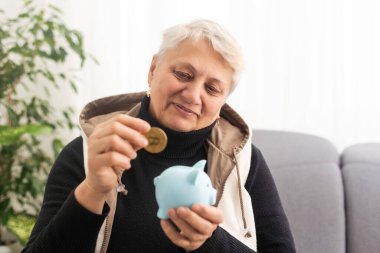 Domuzlu para kutusu tutan yaşlı kadının yakın çekimi. Kıdemli kadın elleri domuz kumbarası tutuyor. Yaşlılık için para biriktirme kavramı
