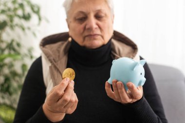 Domuzlu para kutusu tutan yaşlı kadının yakın çekimi. Kıdemli kadın elleri domuz kumbarası tutuyor. Yaşlılık için para biriktirme kavramı
