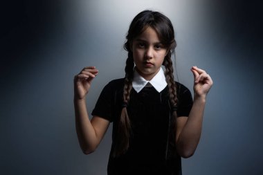 Cadılar Bayramı 'nda Çarşamba Addams kostümlü küçük bir kızın portresi. Ciddi ifade ve karanlık arkaplan ile karanlık atmosfer
