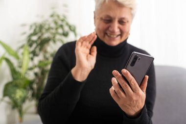 Mutlu, olgun, 60 'lı yaşlarda bir kadın cep telefonuyla video görüşmesi yapıyor, komik videolar izlerken gülüyor, cep telefonuyla piyango teklifini kazanırken heyecanlanıyor evinde koltukta oturuyor..
