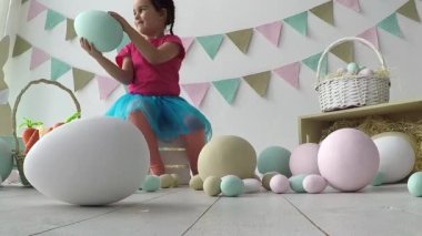 Paskalya küçük kızı paskalya yumurtalarıyla oynuyor, yerde bir sürü paskalya dekoru var.
