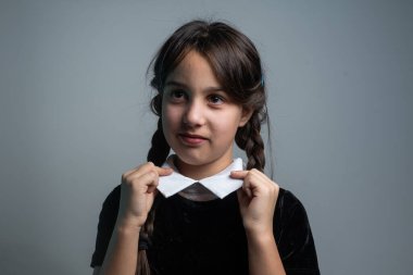 Cadılar Bayramı 'nda Çarşamba Addams kostümlü küçük bir kızın portresi. Ciddi ifade ve karanlık arkaplan ile karanlık atmosfer