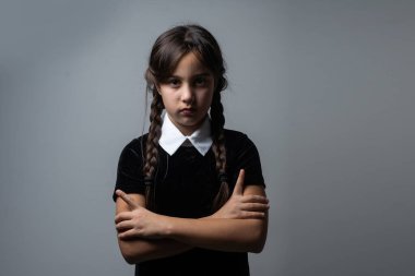 Cadılar Bayramı 'nda Çarşamba Addams kostümlü küçük bir kızın portresi. Ciddi ifade ve karanlık arkaplan ile karanlık atmosfer